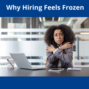 A woman hugging herself to stay warm while sitting at a desk with her laptop, the caption read "Why Hiring Feels Frozen."